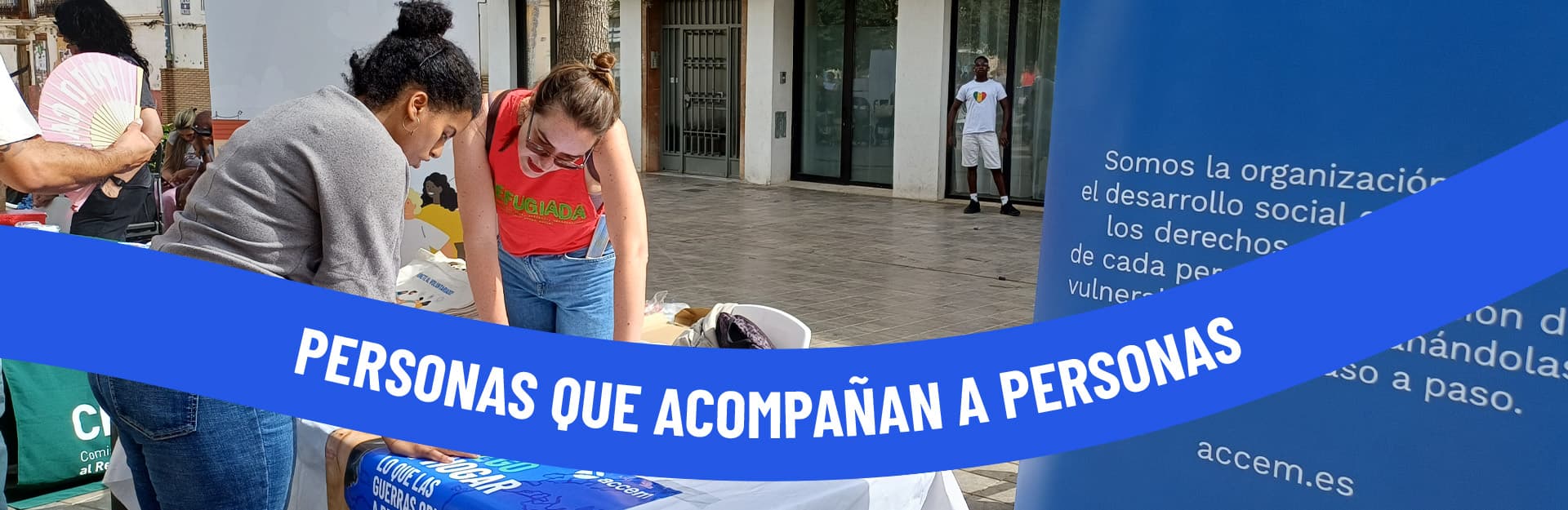 Dos voluntarias de Accem en una mesa informativa en la calle, con el lema «Personas que acompañan a personas»