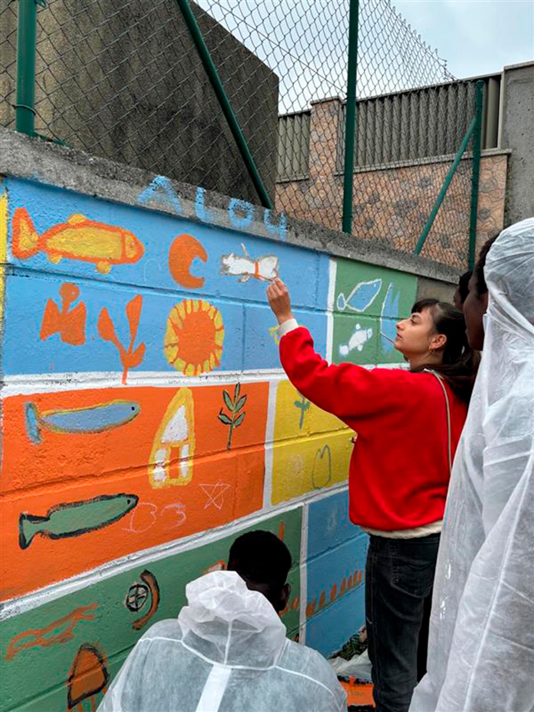 Una voluntaria pinta un mural con peces y flores de colores